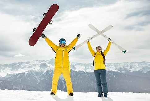 Two skiers in yellow lift their skis and snowboards in the air