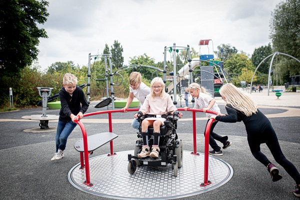 Four children and a girl in a wheelchair playing on the accessible carousel at GIVSKUD ZOO – ZOOTOPIA