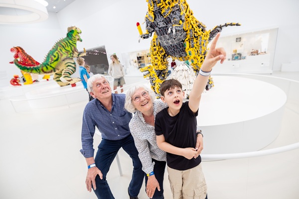 Grandparents are looking at LEGO® dinosaurs together with their grandchild in the LEGO® House