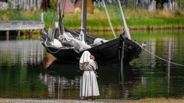 A woman from the Middle Ages stands on the shore with a child in her arms